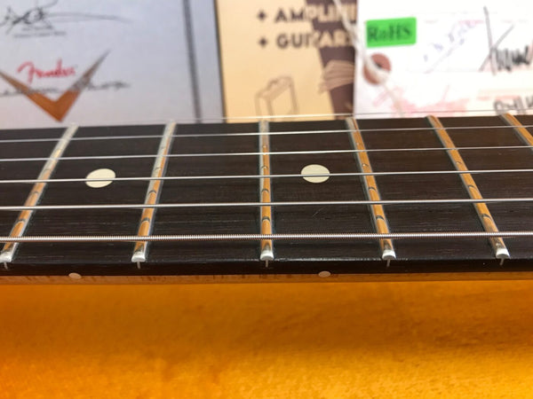 Close-up of guitar fretboard with metal frets and white dot inlays, steel guitar strings, and vintage guitar boxes in background.