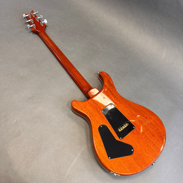 Back side view of a glossy mahogany electric guitar with black plastic control cavity covers and six tuning pegs on a gray background
