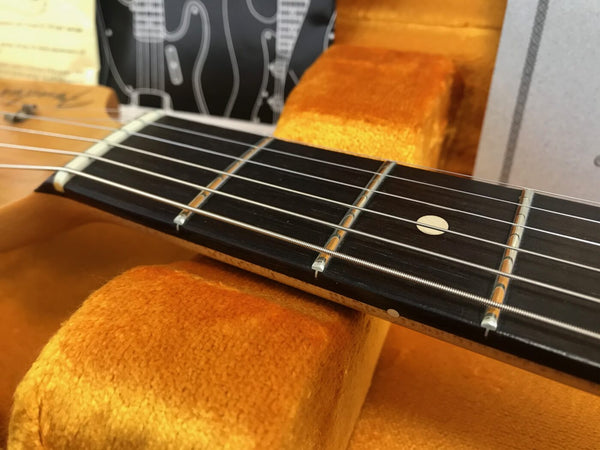 Close-up of guitar neck and fretboard with metal strings and dot inlays resting on orange plush guitar case lining