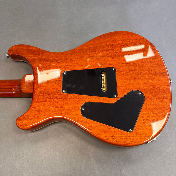 Back side of a polished mahogany electric guitar body with two black plastic cavity covers and visible strings through the bridge cavity