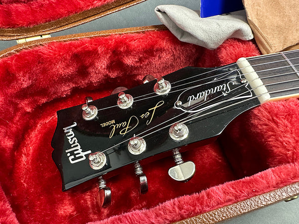 Close-up of Gibson Les Paul Standard guitar headstock with tuning pegs inside red plush-lined guitar case