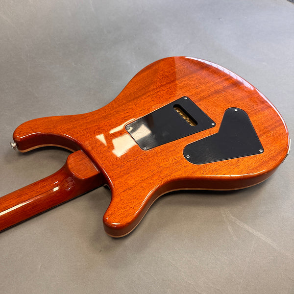 Back side of polished mahogany electric guitar body featuring black plastic control cavity covers on gray surface background