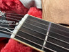 Close-up of acoustic guitar headstock and fretboard showing nut, strings, and first fret in guitar case with red plush lining.