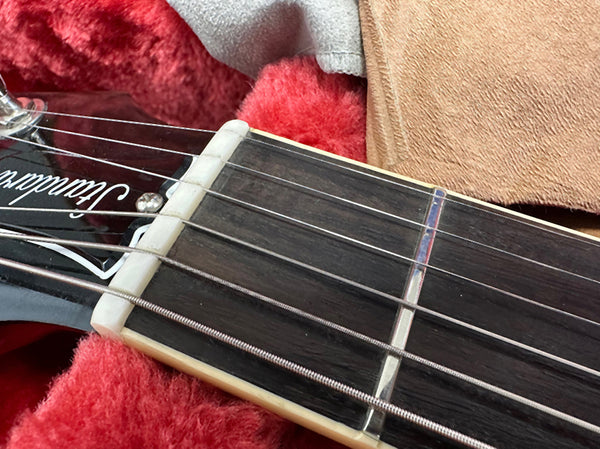 Close-up of acoustic guitar headstock and fretboard showing nut, strings, and first fret in guitar case with red plush lining.