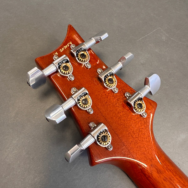 Close-up of mahogany guitar headstock with six silver tuning pegs and gear housings on gray background