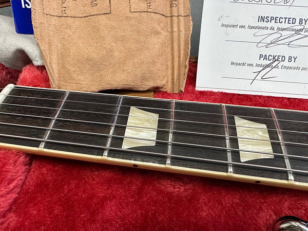 Close-up of guitar fretboard with pearl trapezoid inlays, metal frets, and guitar strings on a rosewood fingerboard with a red plush guitar case interior.