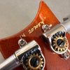 Close-up of guitar tuning pegs and serial number on brown wooden headstock with metal tuning gears