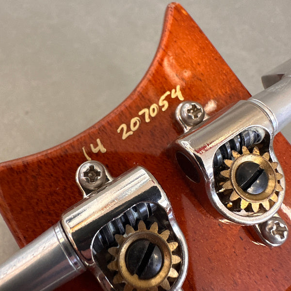 Close-up of guitar tuning pegs and serial number on brown wooden headstock with metal tuning gears
