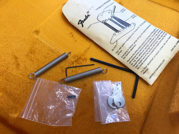 Fender tremolo spring replacement kit with tension screws, hex keys, and instruction envelope on orange fabric background