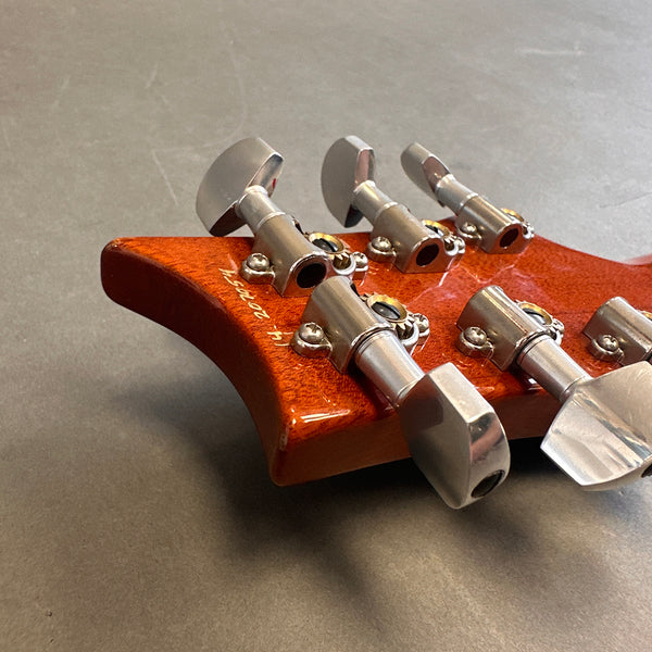 Close-up of guitar tuning pegs on a polished wooden headstock with serial number visible, laid on gray surface