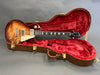 Electric guitar vintage sunburst finish with cream pickguard in open red velvet-lined hard case on gray background
