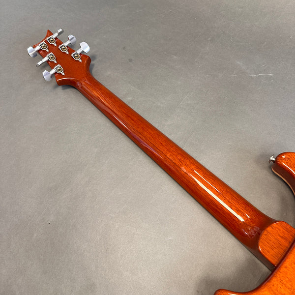 Back view of polished mahogany guitar neck and headstock with chrome tuning pegs on gray background