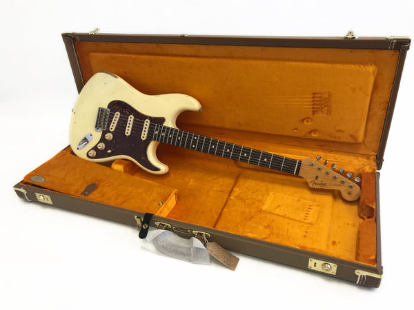 Vintage Fender Stratocaster electric guitar with worn white finish and tortoiseshell pickguard in orange-lined brown hardshell case