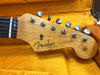 Close-up of Fender Stratocaster electric guitar headstock with tuning pegs and strings in orange plush guitar case interior