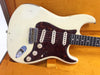 Close-up of vintage white electric guitar with tortoiseshell pickguard, three single-coil pickups, and cream tone and volume knobs inside orange plush guitar case