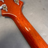 Close-up of glossy mahogany guitar neck with vintage-style tuning pegs on gray background