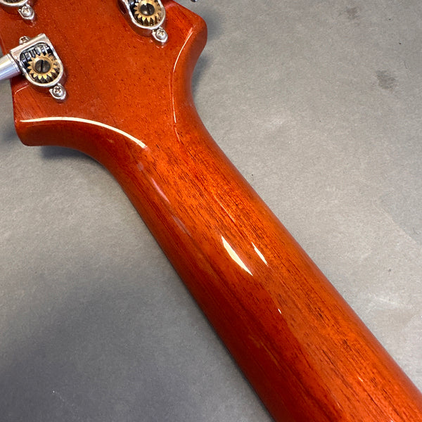 Close-up of glossy mahogany guitar neck with vintage-style tuning pegs on gray background