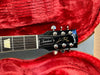 Gibson Les Paul Standard electric guitar headstock with tuning pegs and logo, resting in red plush guitar case