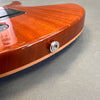 Close-up of mahogany electric guitar body with orange finish and strap button detail on gray background