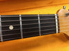 Close-up of electric guitar fretboard showing metal frets, dot inlay, and strings with yellow background