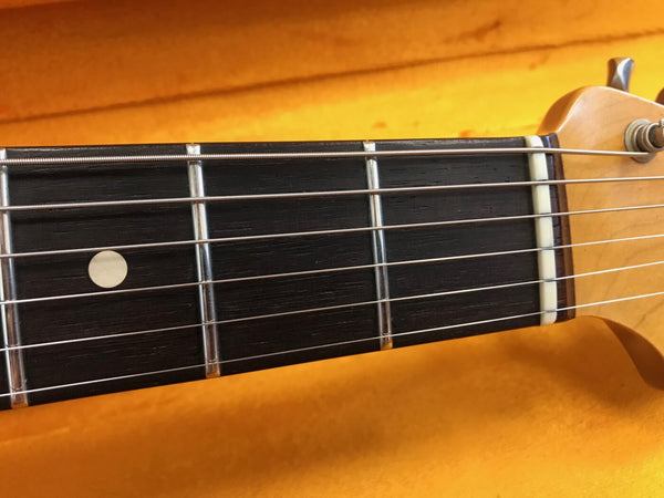 Close-up of electric guitar fretboard showing metal frets, dot inlay, and strings with yellow background