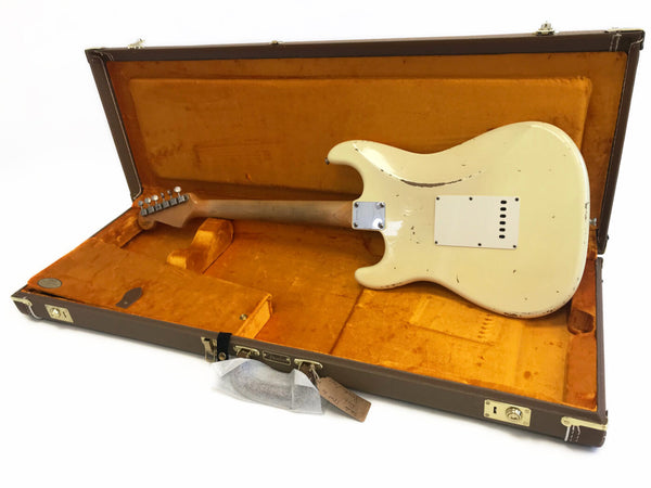 Vintage Fender Stratocaster electric guitar in aged white finish with visible wear, shown from back inside an orange plush lined vintage brown hard case with Fender logo