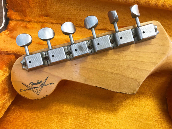 Close-up of vintage Fender Custom Shop guitar headstock with six tuning pegs on a yellow velvet guitar case interior