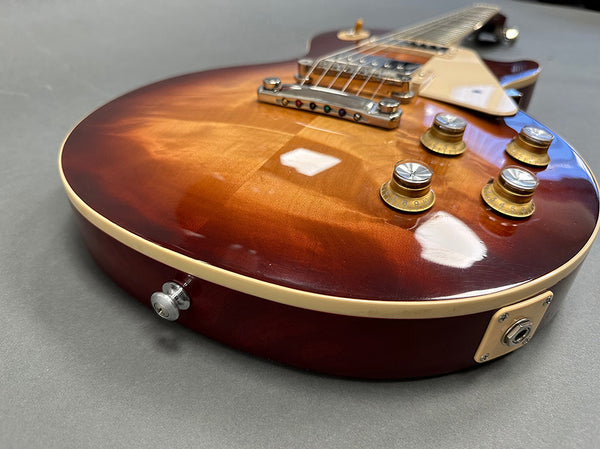 Close-up angled view of sunburst electric guitar body with cream binding, chrome bridge, and gold control knobs on gray background