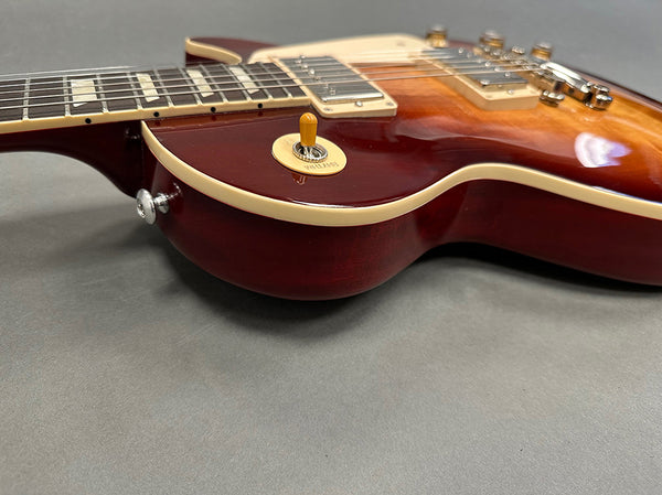 Close-up side view of cherry sunburst electric guitar body with cream binding and toggle switch on gray background