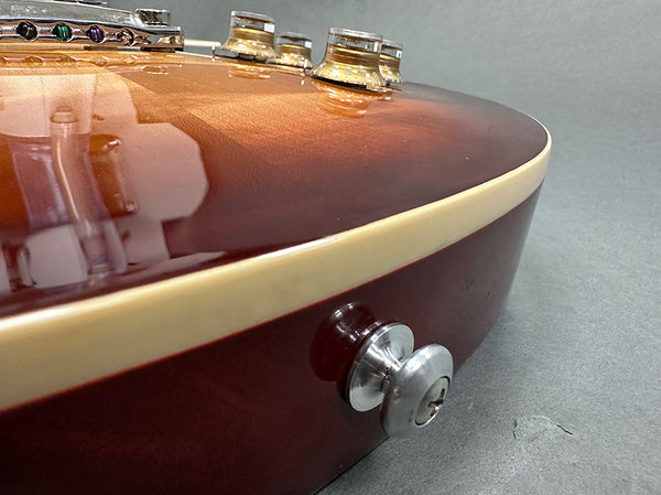 Close-up view of sunburst electric guitar body showing cream binding, chrome strap button, and control knobs on gray background