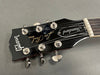 Close-up of Gibson Les Paul Standard guitar headstock with six tuning pegs and black finish on grey background