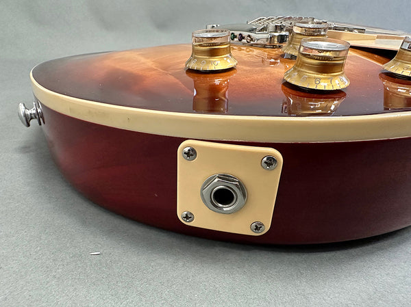 Close-up of vintage sunburst electric guitar body showing input jack, volume and tone control knobs, and cream binding on a gray surface