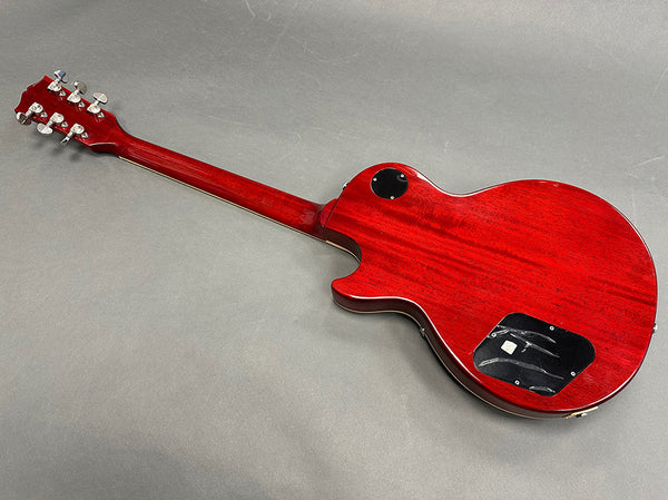 Back view of red electric guitar with solid wood body and chrome tuning pegs on gray background