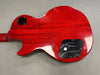 Back of red electric guitar showing wood grain and black plastic control cavity covers on gray background.