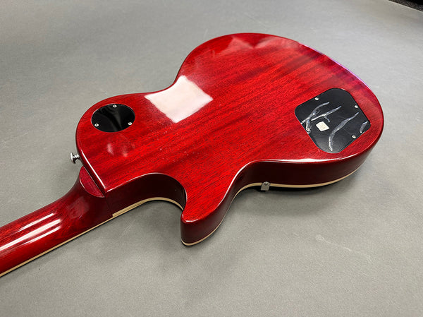 Back view of a red electric guitar body with glossy finish and cream binding on a gray surface