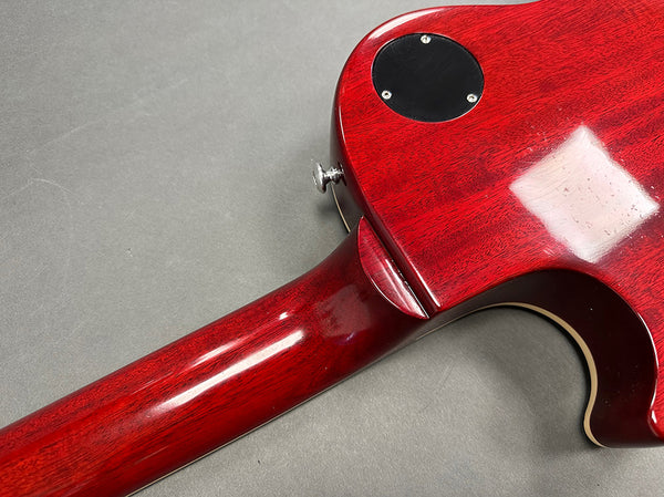 Close-up view of the back of a red electric guitar neck and body joint with glossy finish and black control cavity cover on a gray background