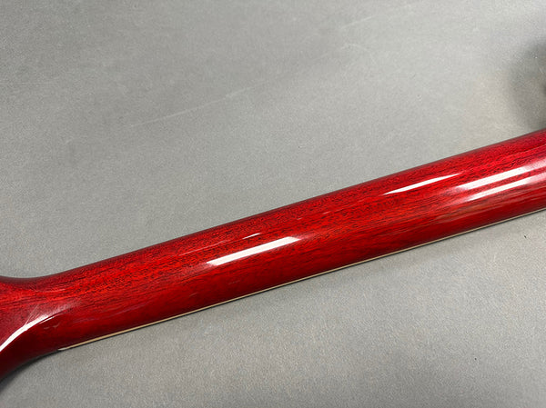 Close-up of a glossy red wooden guitar neck showing detailed wood grain and smooth finish on gray background.