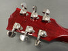Close-up of red guitar headstock with six silver tuning pegs and visible serial number stamped on wood, showing back of guitar tuners for precise string adjustment