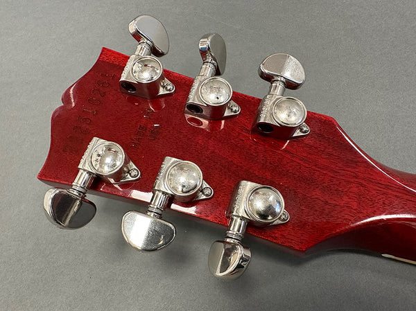 Close-up of red guitar headstock with six silver tuning pegs and visible serial number stamped on wood, showing back of guitar tuners for precise string adjustment
