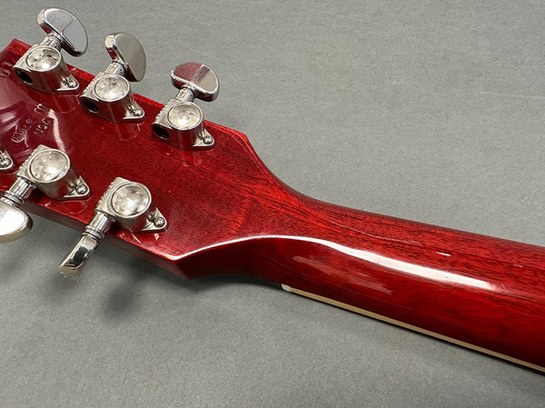 Close-up of red wooden guitar headstock with silver tuning pegs and gray background, Coffee House Guitars product image