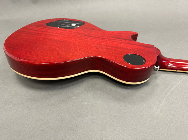 Back view of cherry red electric guitar body with cream binding and black control cavity covers on gray background