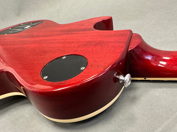 Close-up of red electric guitar back body showing control cavity cover and strap button on gray background