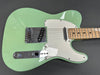 Close-up of a seafoam green electric guitar with maple neck, white pickguard, and chrome hardware on a gray background