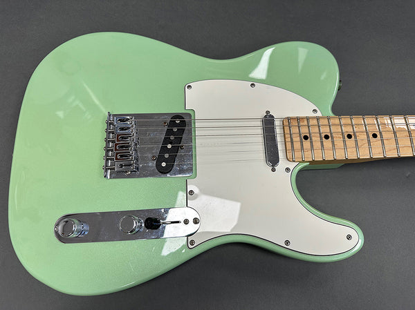 Close-up of a seafoam green electric guitar with maple neck, white pickguard, and chrome hardware on a gray background