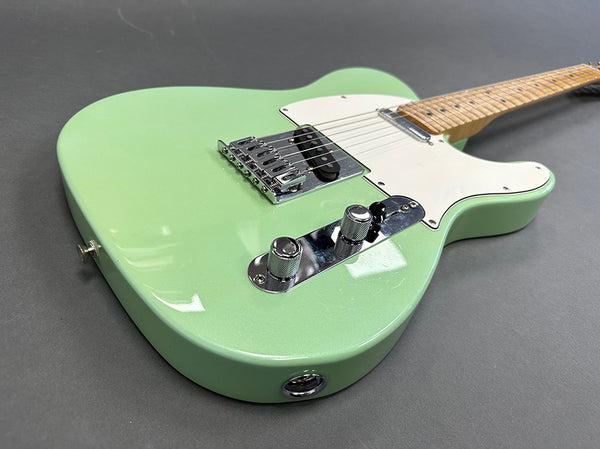 Close-up of seafoam green electric guitar with white pickguard and maple neck on gray background