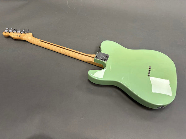 Back view of light green electric guitar with maple neck and chrome tuning pegs on gray background.