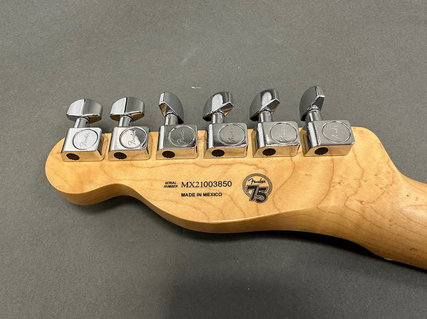Close-up of Fender electric guitar headstock back with six chrome tuning pegs, serial number MX21003850, made in Mexico, and Fender 75th anniversary logo.
