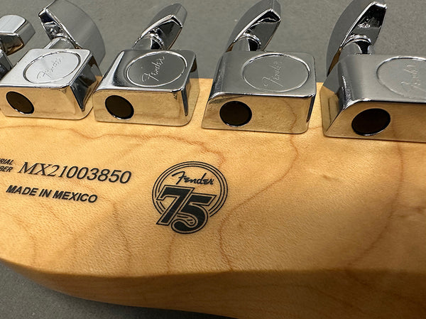 Close-up of Fender guitar headstock featuring chrome tuning pegs, serial number MX21003850, "Made in Mexico" stamp, and Fender 75th anniversary logo on maple wood.