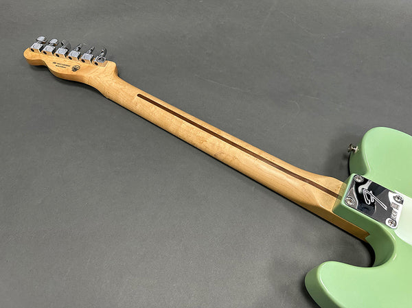 Maple guitar neck with skunk stripe and chrome tuning pegs on seafoam green Fender electric guitar body on gray background