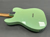 Back side of a mint green electric guitar with a maple neck and chrome hardware on a gray surface